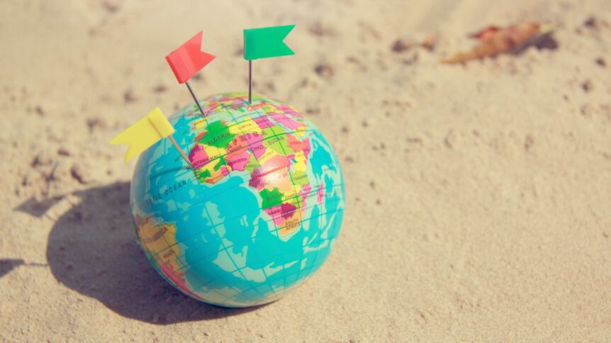 Pin marks on different destinations on a globe that is on beach